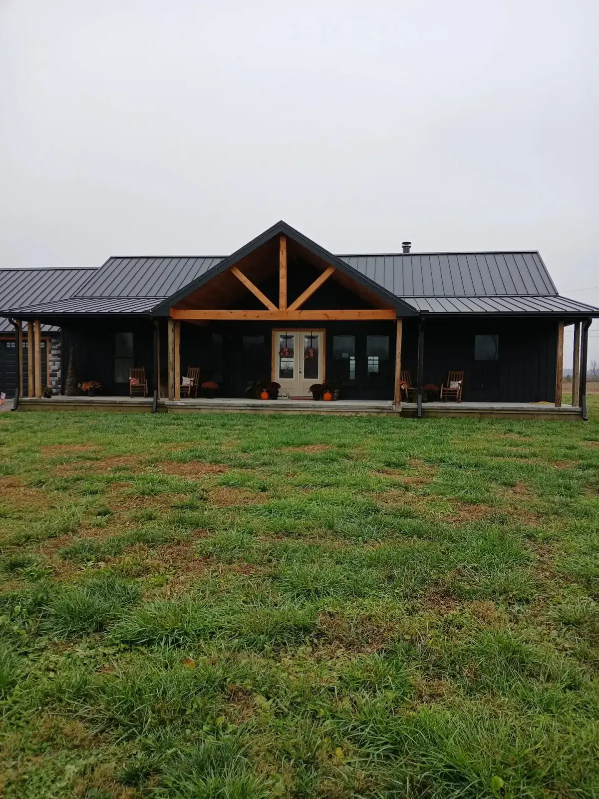 Black barndominium with a standing seam metal roof, timber gable truss and full-width porch