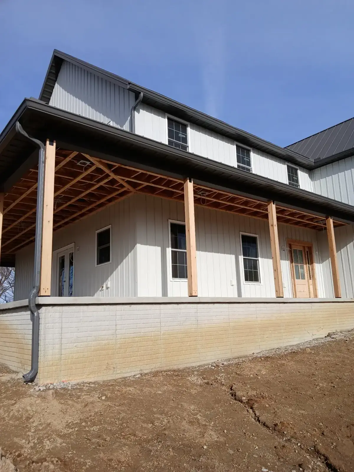 Two-storey home in light grey board and batten metal siding with an unfinished timber porch