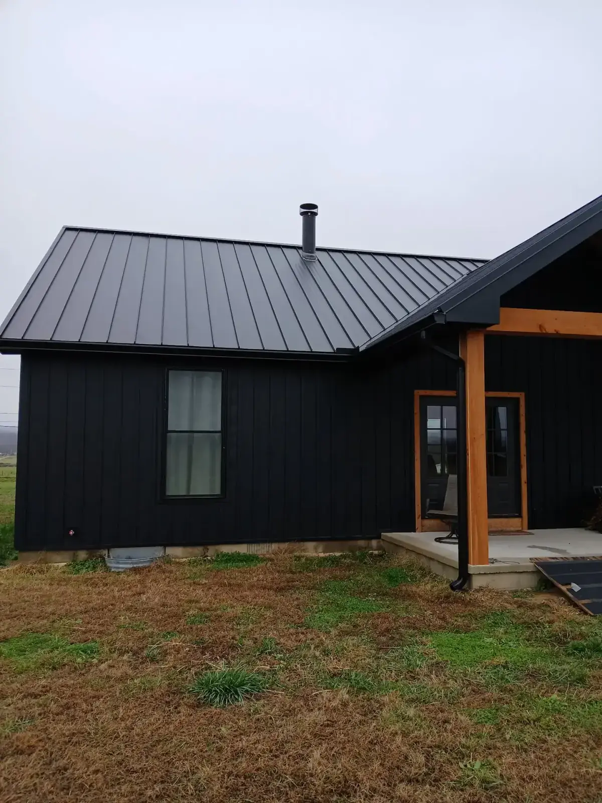 Gable end of a black metal roof and matching board and batten siding with a stove pipe