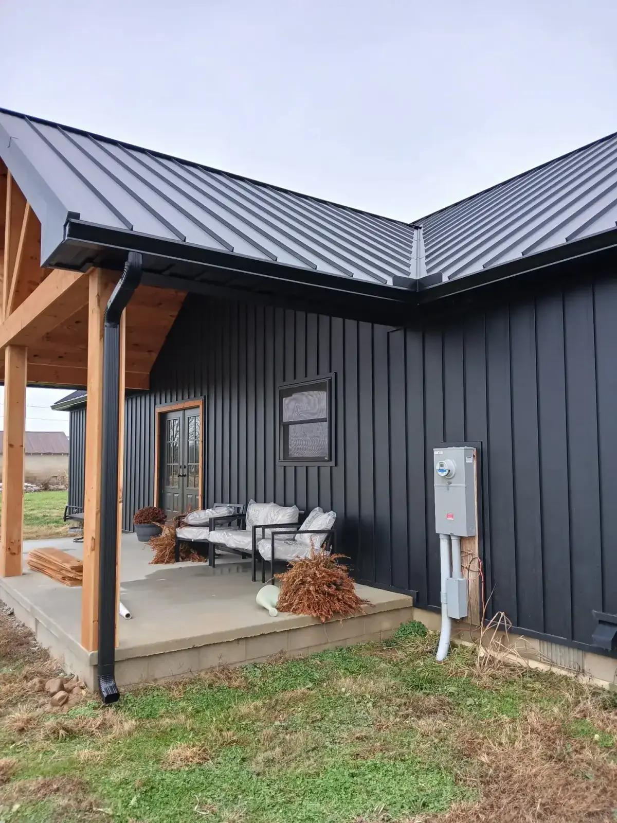 Corner of a black standing seam roof meeting board and batten metal siding above a covered porch