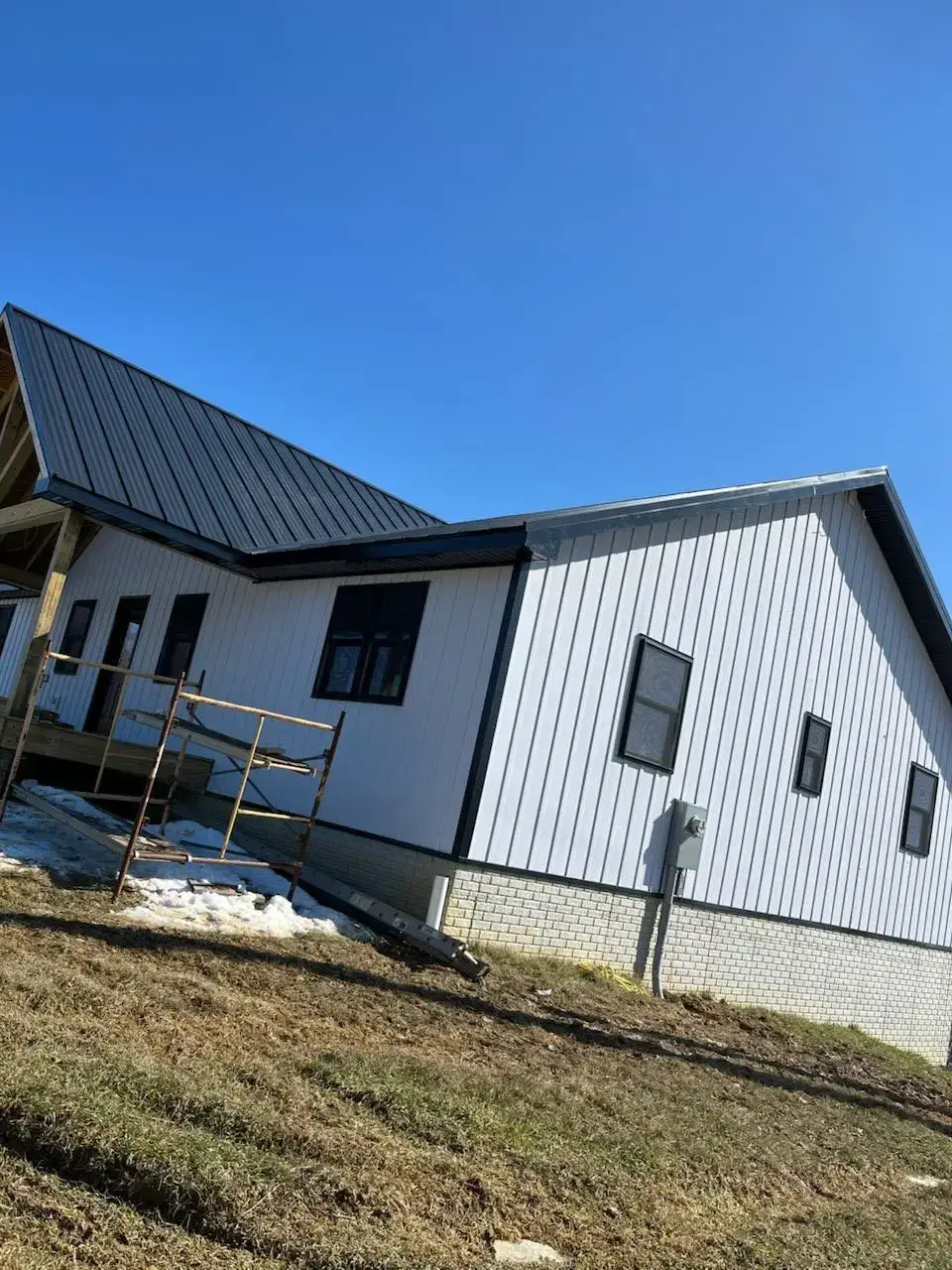 Scaffolding against a house with a new black standing seam roof and white siding