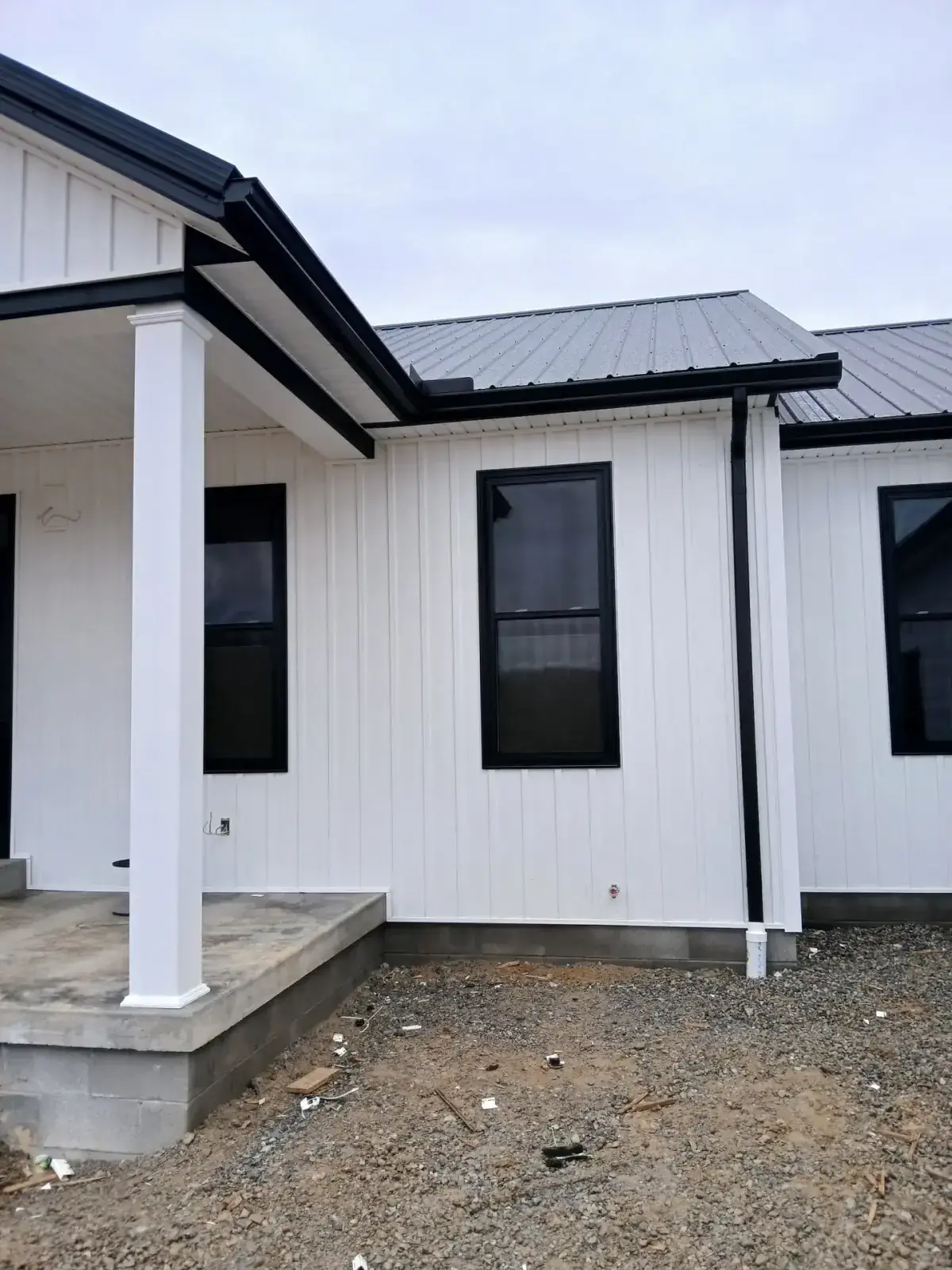 Black gutter and downspout against white board and batten metal siding